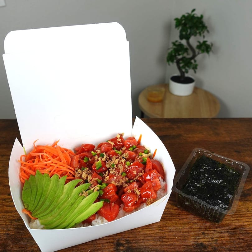 A Sushi Box TB poke bowl with tuna, avocado, carrots, and nori on a wooden table.